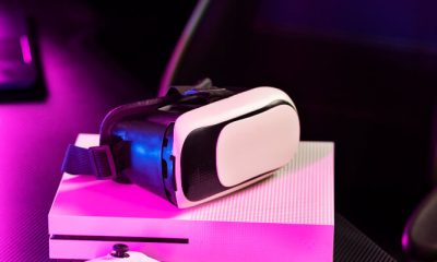 A PS5 controller on a table with a VR glass on top of a PS console in an illuminated room.